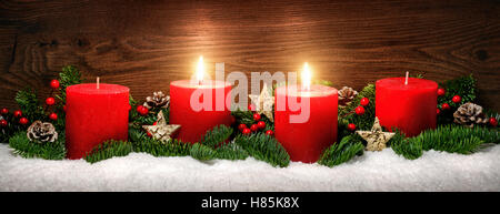 Discrète, studio shot élégant de la décoration de l'avent avec des branches de sapin sur la neige et de remorquage de brûler des bougies rouges, fond en bois sombre. Banque D'Images