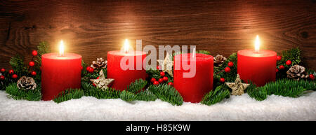 Discrète, studio shot élégant de la décoration de l'avent avec des branches de sapin sur la neige et trois bougies rouges en feu, fond en bois sombre. Banque D'Images