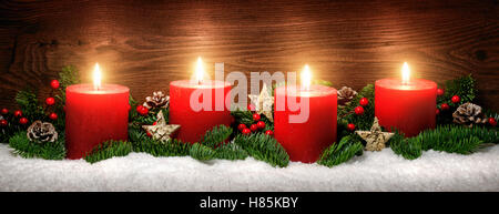 Discrète, studio shot élégant de la décoration de l'avent avec des branches de sapin sur la neige et quatre bougies rouges en feu, fond en bois sombre. Banque D'Images