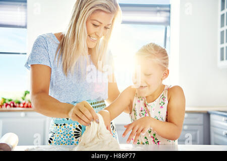 Petite fille s'amusant d'aider dans la cuisine apprendre à cuire avec son tendre mère qu'ils pétrissent la pâte ensemble b rétroéclairé Banque D'Images