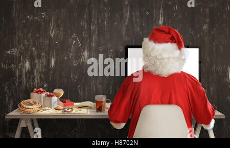 Le Père Noël se prépare pour un voyage et le partage des cadeaux sur ordinateur. À côté sur la table est une carte, boussole, sablier, livre avec l'instr Banque D'Images