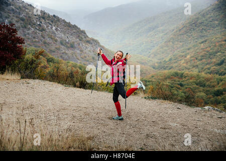 Jeune fille touriste avec les bâtons de marche de jouer sur un sentier de montagne dans la pluie au cours de la Crimée marathon de montagne Banque D'Images