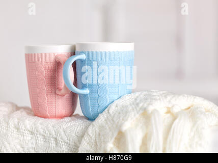 Couple de tasses avec knitting pattern, sont de couleur rose et bleu sur la couverture en tricot blanc chaud. Banque D'Images