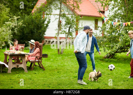 Les amis jouent au football avec chien au jardin d'été Banque D'Images