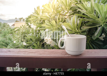 Tasse de café avec cuillère à café sur le balcon en bois avec du soleil le matin et nature background Banque D'Images