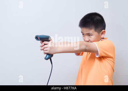 Asian boy but une fausse arme réalisée avec lecteur de codes à barres, studio shot, sur fond de mur gris avec soft shadow Banque D'Images