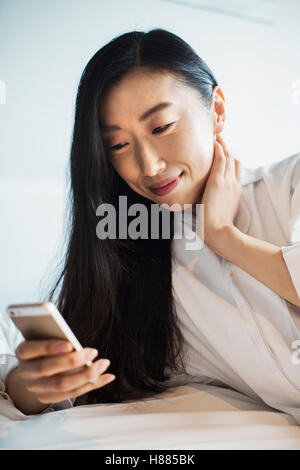 Une femme d'affaires préparation au travail, assis au lit à l'aide de son téléphone intelligent. Banque D'Images