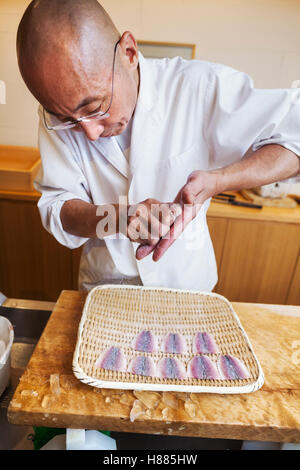 Un chef cuisinier travaillant dans une petite cuisine commerciale, un maître itamae ou chef making sushi, préparer un poisson. Banque D'Images