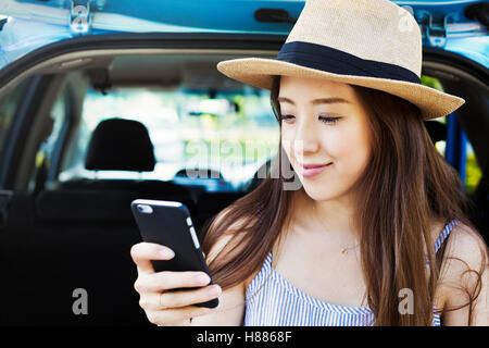 Jeune femme avec de longs cheveux bruns, portant chapeau de Panama, à l'aide d'un téléphone mobile. Banque D'Images