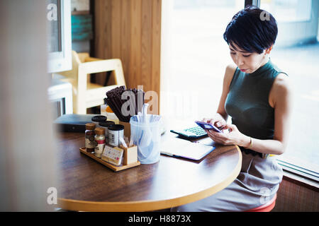 La boutique de nouilles ramen. Une femme assise à une table à l'aide de son téléphone intelligent. Banque D'Images