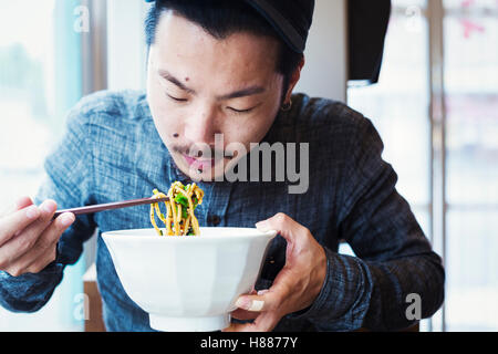 Un café de nouilles ramen dans une ville. Un homme assis manger nouilles ramen à partir d'un grand bol de bouillon. Banque D'Images