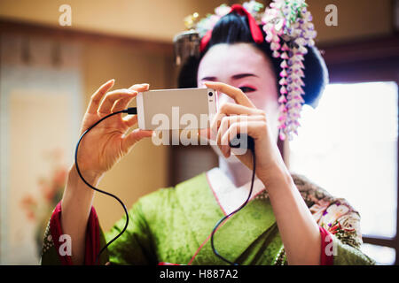 Une femme vêtue de la traditionnelle style geisha, vêtu d'un kimono et obi, avec une coiffure élaborée en tenant un. selfies Banque D'Images