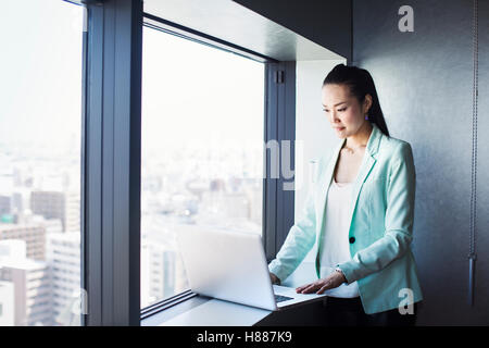 Une femme d'affaires par une fenêtre en utilisant son ordinateur portable. Banque D'Images