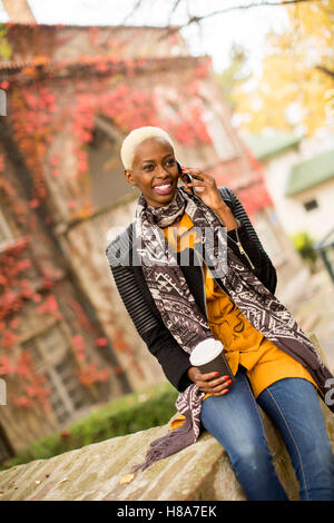 Jolie jeune femme noire avec une tasse à café et téléphone mobile Banque D'Images