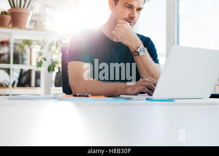 Tourné à l'intérieur du jeune homme assis à une table et de travailler sur ordinateur portable. L'homme d'affaires à l'aide d'un ordinateur portable tout en étant assis à son bureau. Banque D'Images