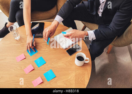 Vue aérienne de deux collègues d'affaires assis à une table et préparant des post-it. Professionnels en brainstorming avec de l'adhésif Banque D'Images
