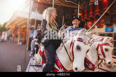 Smiling man and woman on amusement park carousel. Jeune couple sur l'carousel ride au parc des expositions. Banque D'Images