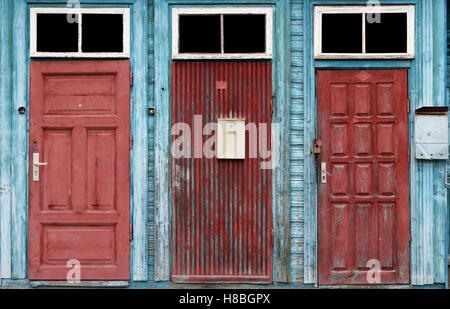 Trois pelés rouges rétro craquelé bleu des portes dans la maison en bois. Windows verre isolé sur fond noir avec patch Banque D'Images