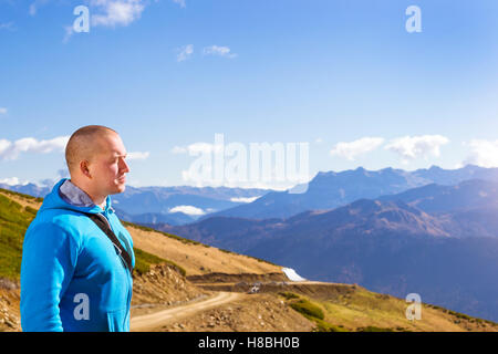 Jeune homme athlétique vêtu d'un sweat bleu, admire de l'automne paysage de montagne, vue sur collines et sommets des montagnes du Caucase Banque D'Images