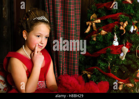 La princesse d'hiver - pensive cute little girl in red dress se félicite de nouvel an et de Noël à l'intérieur de charme Banque D'Images