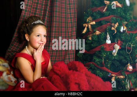 La princesse d'hiver - pensive cute little girl in red dress se félicite de nouvel an et de Noël à l'intérieur de charme Banque D'Images