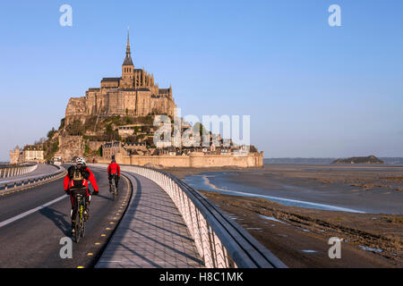 Mont Saint-Michel (Saint Michael's Mount), (Normandie, nord-ouest de la France) : les cyclistes sur la passerelle. Banque D'Images