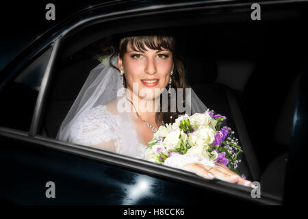 Beautiful smiling bride avec un bouquet de mariage dans la fenêtre de voiture Banque D'Images