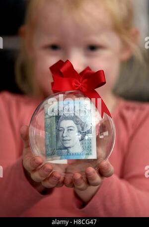 Un bébé fille tenant une boule de Noël avec une note de cinq livres à l'intérieur. Banque D'Images