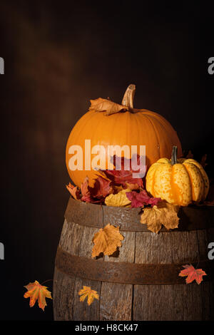 Pumpkins assis sur tonneau en bois rustique avec des feuilles d'automne Banque D'Images