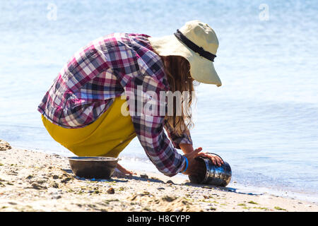 Jeune fille au chapeau du soleil assis sur son derrière et se lave à l'échelle bowler de manger. Marmite. Banque D'Images