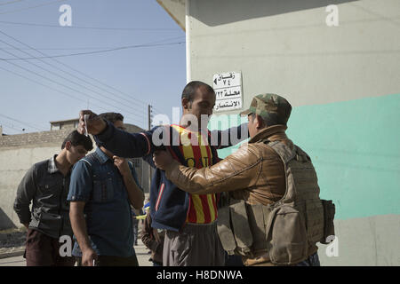 Mossoul, Ninive, de l'Iraq. Nov 11, 2016. 11/11/2016. Mossoul, Irak. Un soldat de l'armée iraquienne's 9e Division blindée, cherche un homme dans le quartier de Mossoul Al Intisar en tant que résidents d'attente à recevoir de la nourriture à partir de volontaires locaux. Le quartier Al Intisar a été prise il y a quatre jours, par les forces de sécurité irakiennes (FSI) et, malgré sa proximité de combats en cours entre l'ISF et de l'ISIS militants, de nombreux habitants vivent toujours dans le règlement sans l'énergie et l'eau ordinaire et avec la diminution des approvisionnements alimentaires. Credit : ZUMA Press, Inc./Alamy Live News Banque D'Images