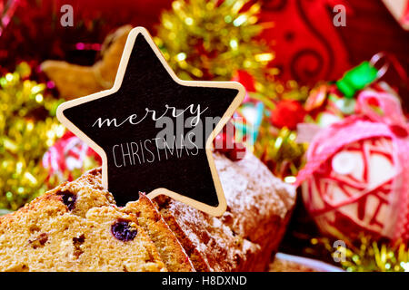 Libre de fruitcake surmontée d'une pancarte en forme d'étoile avec le texte joyeux noël, sur une table pleine de cadeaux de Noël et Banque D'Images