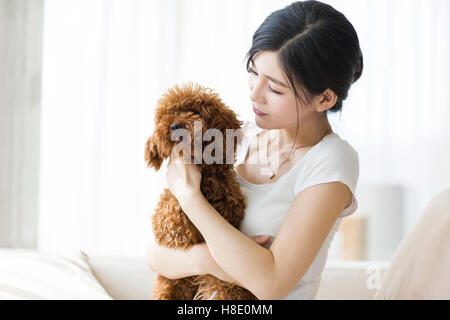 Jeune femme chinoise à jouer avec un animal de compagnie à la maison caniche Banque D'Images