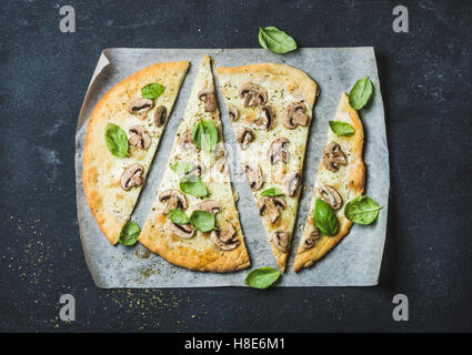 Pizza aux champignons fait maison avec du basilic coupé en tranches sur du papier sulfurisé sur fond noir en noir, vue du dessus, composition horizontale Banque D'Images