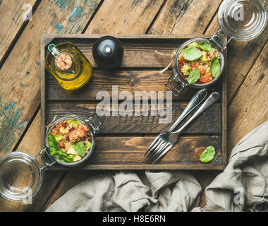 Maison saine Salade de quinoa au bol en verre de cherry et de tomates séchées au soleil, avocat, basilic, dans un coffret en bois au fond rustique, Banque D'Images