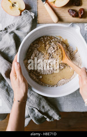 Une femme est photographié alors qu'elle se plie aux ingrédients secs dans les ingrédients liquides pour une pâte à muffins apple. Banque D'Images