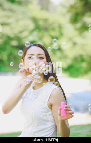 Jeune japonaise soufflant des bulles de savon dans un parc de la ville Banque D'Images