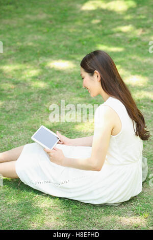 Portrait de jeune japonaise portant sur l'herbe avec tablet Banque D'Images