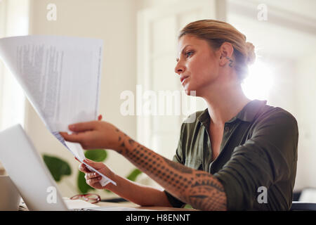 Portrait de belle jeune femme assise à table et la lecture de documents. Femme passant par quelques formalités administratives à la maison. Banque D'Images