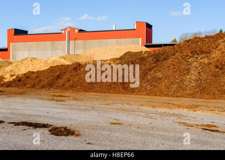 Gros tas de biomasse combustible solide sous forme de copeaux de bois de taille moyenne. Bâtiment industriel en arrière-plan Banque D'Images