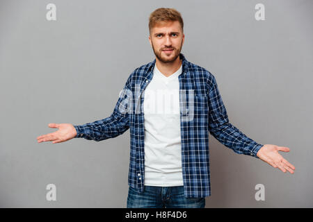 Portrait d'un homme barbu en haussant les épaules isolé sur fond gris Banque D'Images
