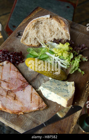 Plowman's déjeuner sur un plateau en bois avec cheeese, du jambon, du pain et des cornichons. Banque D'Images