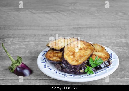 Aubergines frites sur une assiette blanche, fond en bois gris. Banque D'Images