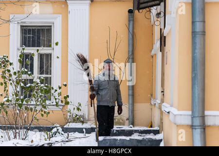 Moscou, Russie. Samedi 12 Novembre, 2016. Au début de l'hiver à Moscou. Pas de soleil, ciel nuageux. Le gel léger jusqu'à -5 degrés Celsius ( +23F) par le soir, neige stable, mais pas très lourd. Un homme dans son âge avec un balai en bois dans la main s'en tient à l'entrée du petit bâtiment de couleur jaune. Ce n'est pas un balai pour nettoyer, c'est de voler ! Crédit : Alex's Pictures/Alamy Live News Banque D'Images