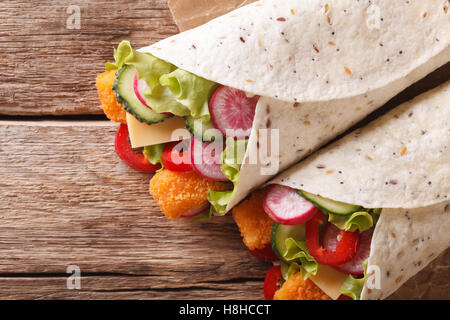 Rouler la tortilla avec les bâtonnets de poisson, fromage et légumes close-up sur la table horizontale vue du dessus. Banque D'Images