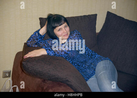 Plump mature femme brune aux yeux clairs dans les jeans et un chemisier est posant avec pigeonneaux sur canapé . Banque D'Images
