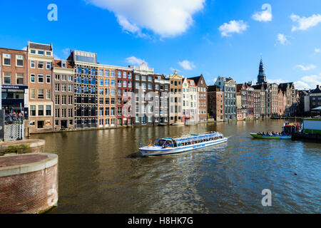 Un bateau-motors le long en face de la fameuse maisons bordant le bord du bassin du canal, Damrak Amsterdam, Pays-Bas Banque D'Images