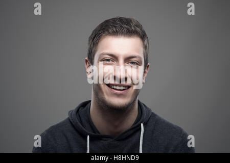 Jeune homme portant capuche sportif et souriant à la caméra à l'arrière-plan gris plus Banque D'Images