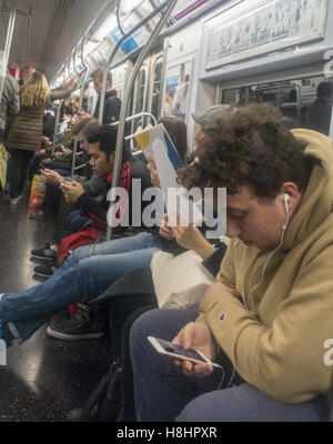 Les personnes qui utilisent leurs téléphones portables sur le train R à Brooklyn, New York. Banque D'Images