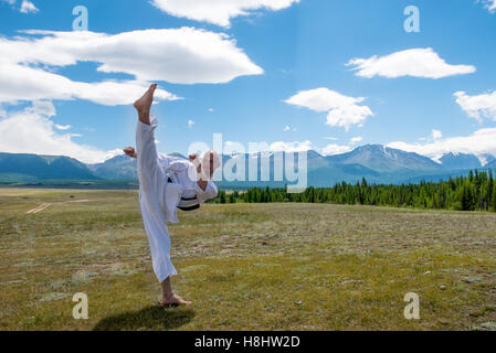 L'homme en kimono blanc et ceinture noire de karaté de formation sur fond de montagne. Banque D'Images